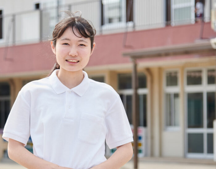 ちくみ幼稚園の園舎の前に立ち、ほほえむりりか先生