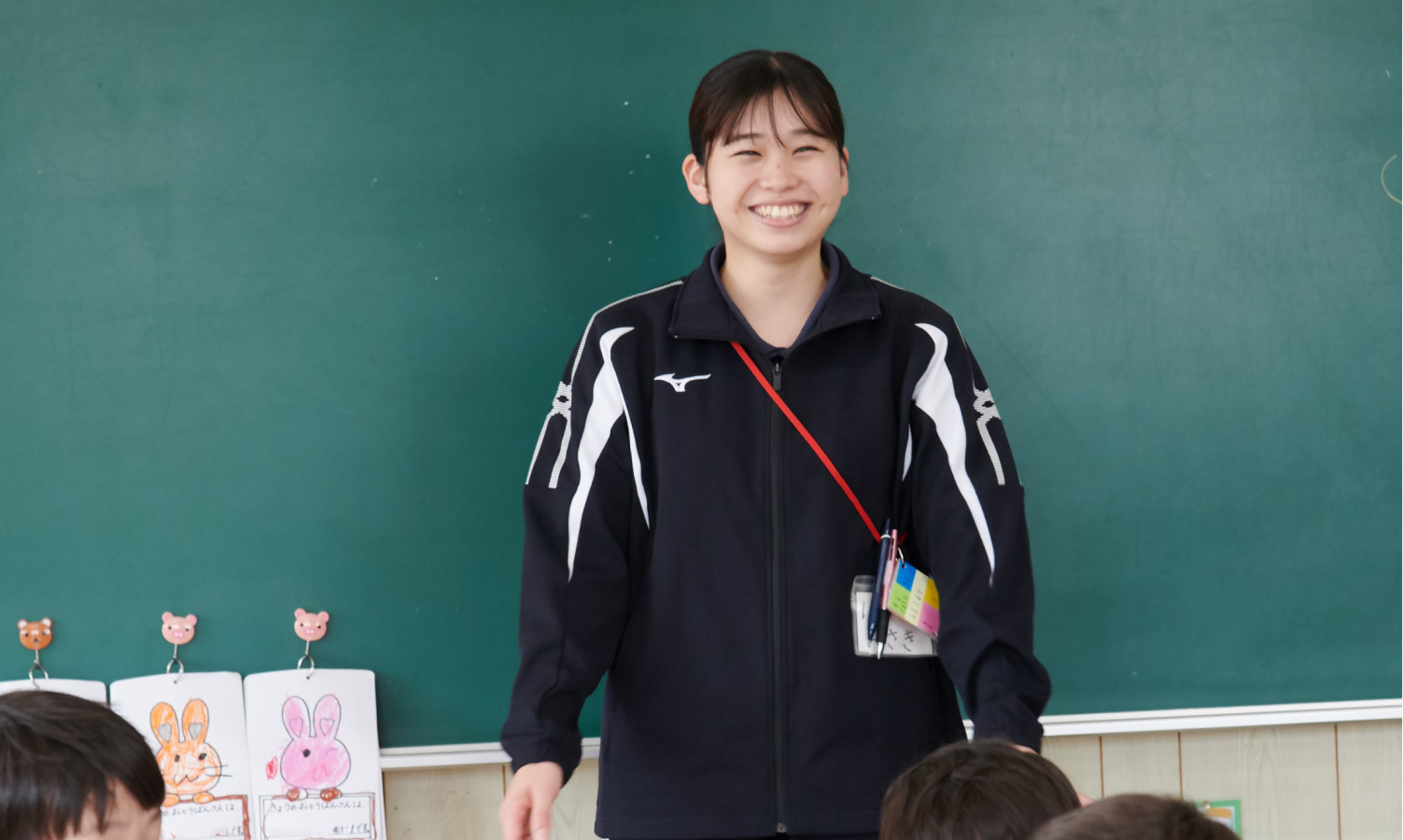 黒板の前に立ち、子どもたちに笑顔で話しかけるみさき先生