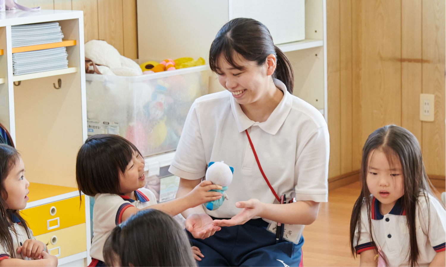 保育室で子どもたちと輪になり、ぬいぐるみを受け取ってほほえむみさき先生