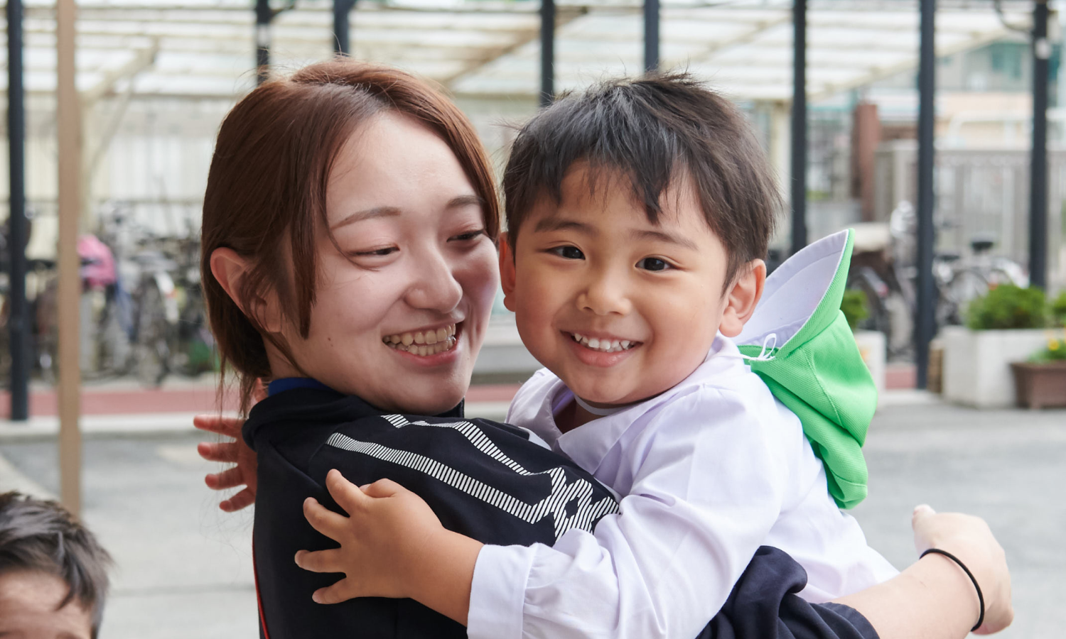 園庭で子どもを抱きかかえ、顔を寄せ合って笑うもえ先生