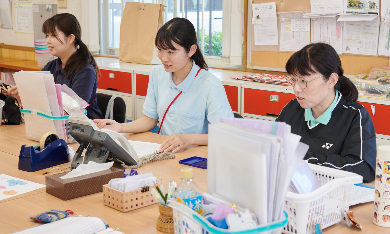 職員室で先生たちと机を囲み、打ち合わせをするりりか先生