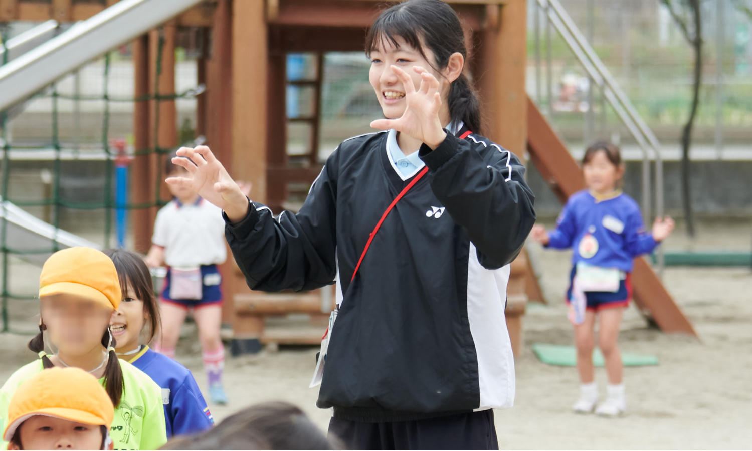 園庭で両手を広げ、身ぶりをつけて子どもたちと運動するりりか先生