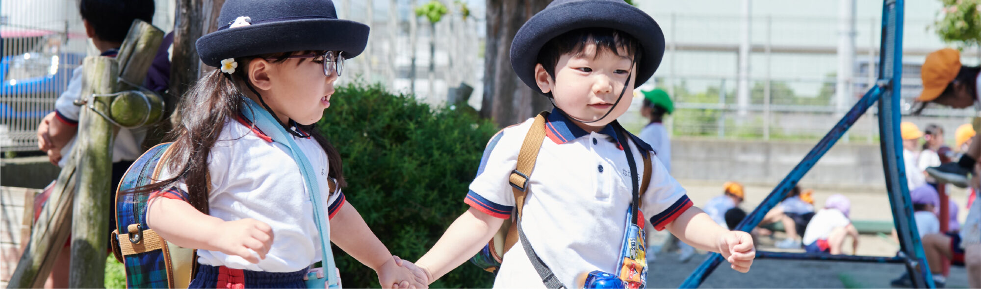 帽子をかぶりカバンをさげて、手をつないで歩く男の子と女の子